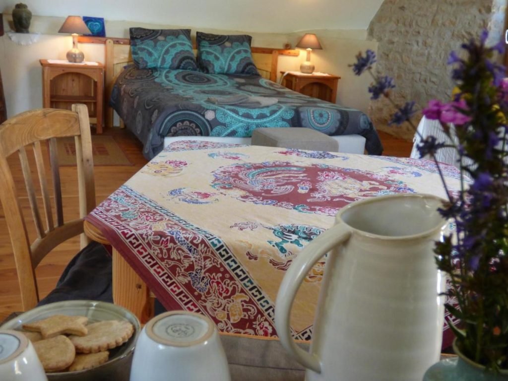 Chambre d’hôtes lumineuse à La Shamballa avec lit double et table de petit-déjeuner, dans un cadre calme et naturel.